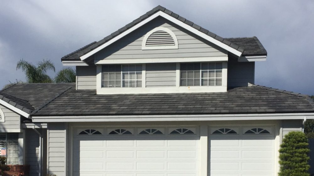 A two-story gray house with a dark tile roof and a white garage, under a cloudy sky.